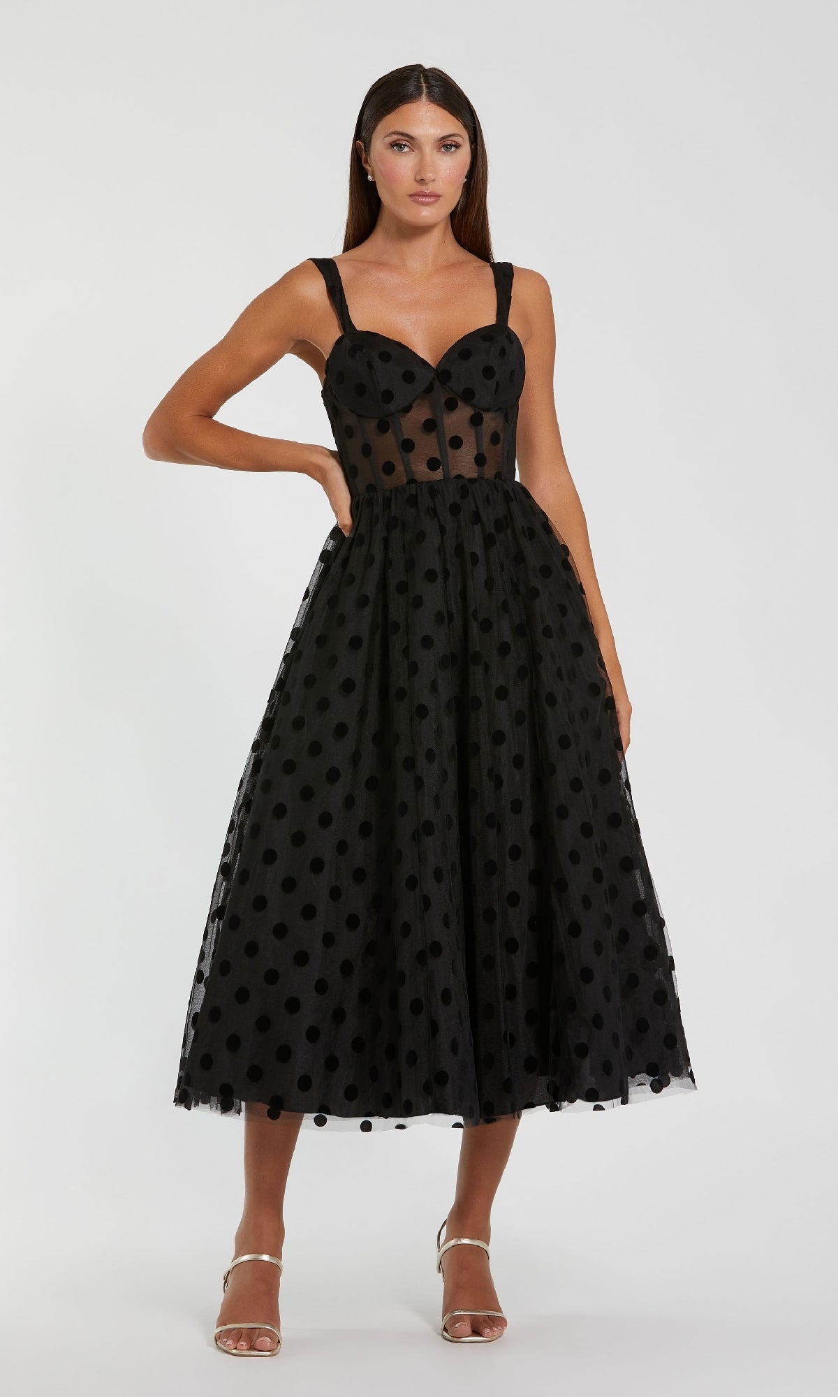 A woman wears the Mac Duggal 27539 Black Midi Polka Dot Party Dress, featuring a sheer overlay and sweetheart neckline, standing against a plain white background.